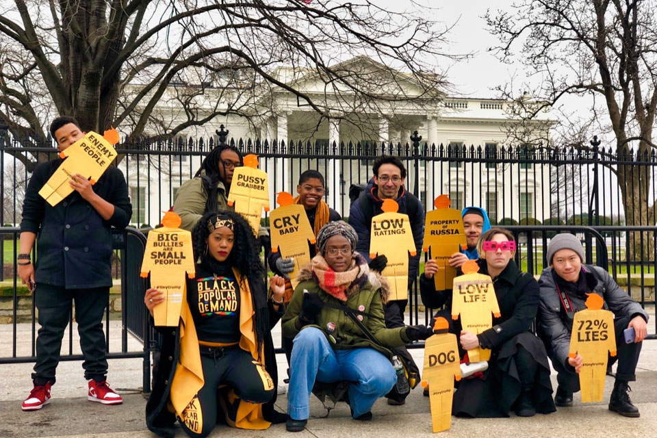 12 project participants standing in front of the White House holding tiny trumps