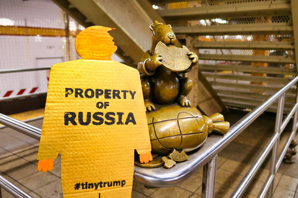 tiny trump with the stamp 'Property of Russia' in the 14th street subway station next to Tom Otterness sculpture of a moneybag