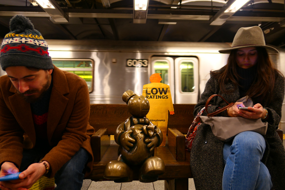'Low Ratings' tiny trump on a nyc subway bench in between two straphangers