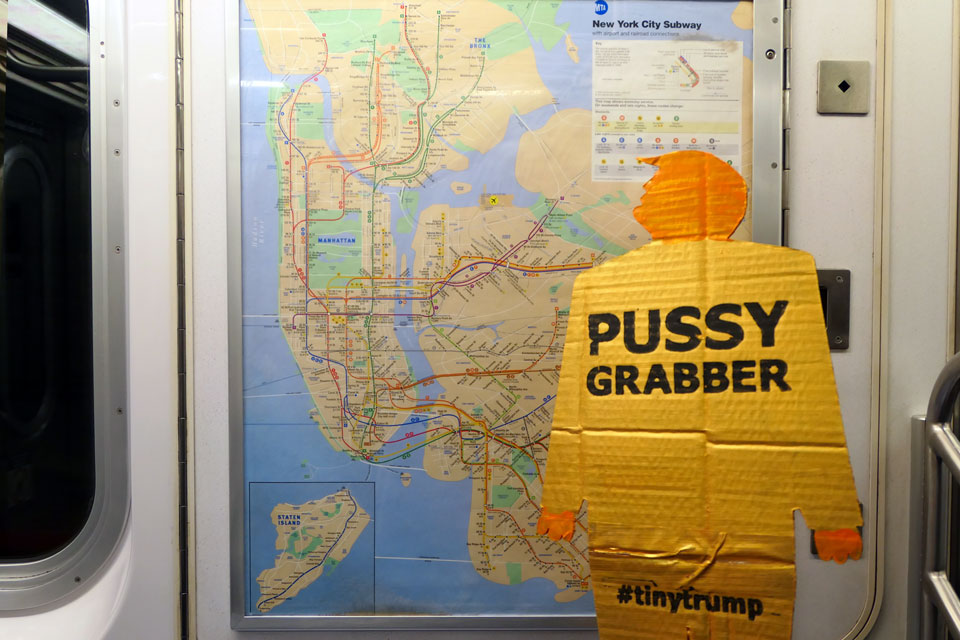 tiny trump with a 'Pussy Grabber' stamp on the NYC subway looking at the MTA subway map