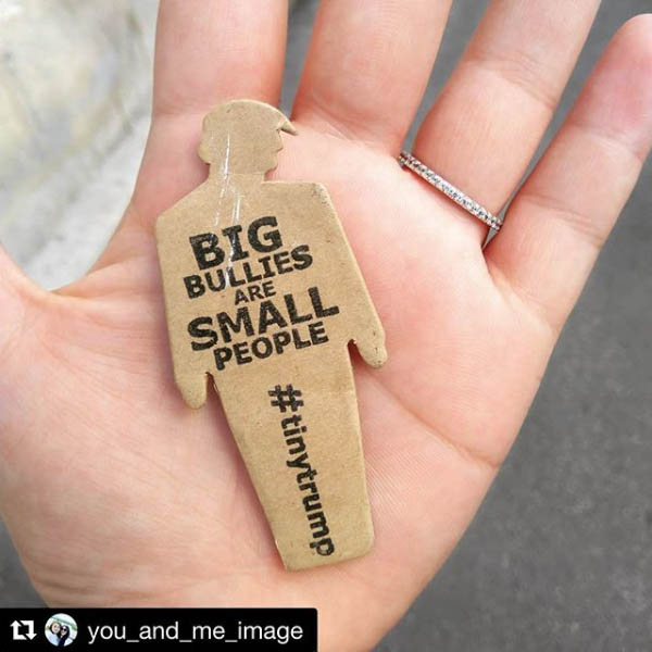 tiny trump with the stamp 'Big Bullies Are Small People' being held in the palm of someone's hand