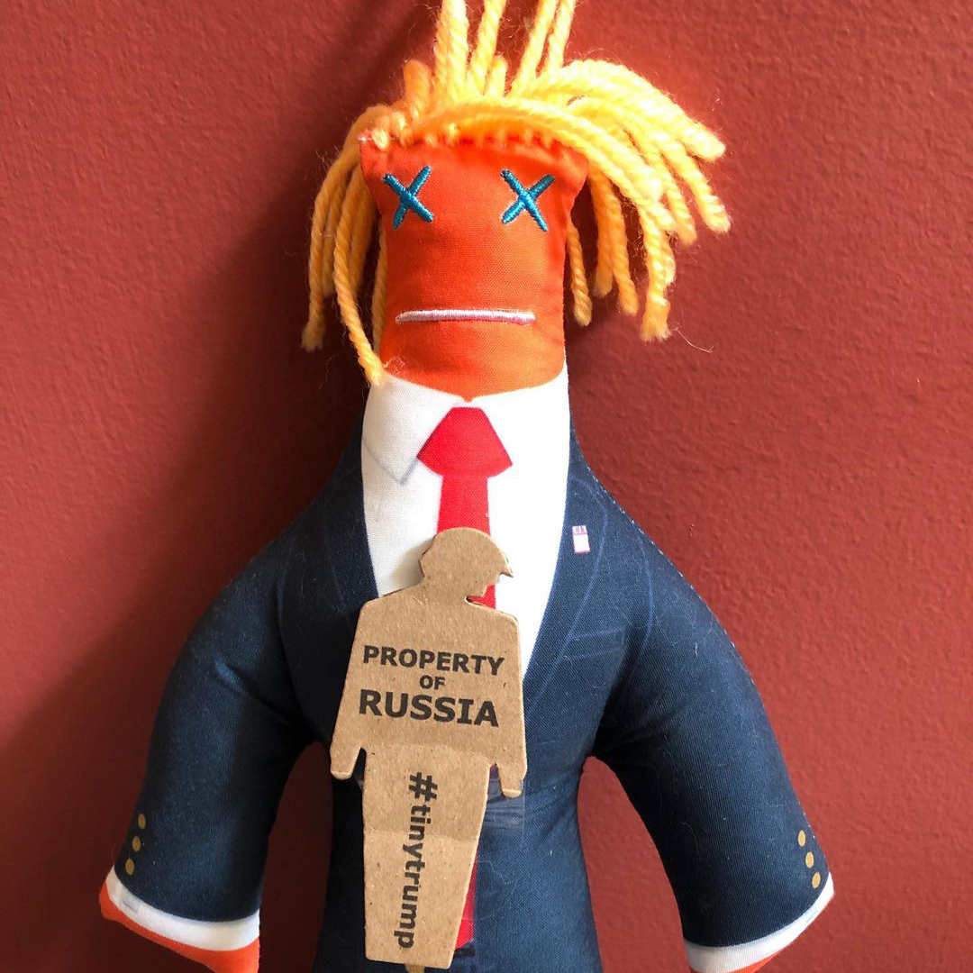 tiny trump with a Property Of Russia slogan stuck to a voo-doo doll version of himself 